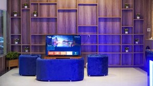 A modern living room with a large flat-screen TV, blue upholstered seating, and wooden shelving with potted plants. - Laylati Al Nagah (Riyadh)