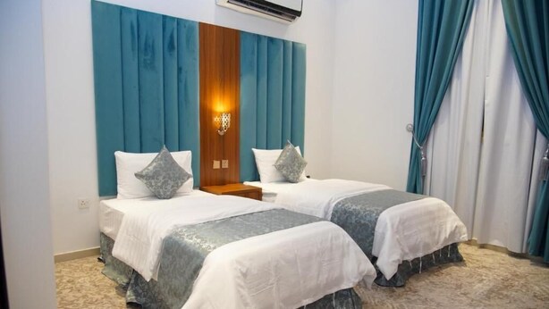 A hotel room with two beds, a wooden headboard, a wall-mounted air conditioner, and a patterned carpet. - Laylati Al Nagah (Riyadh)
