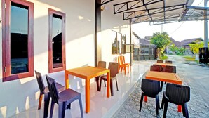 A covered outdoor seating area with tables and chairs, a glass door entrance, and a view of the surrounding area. - OYO 90618 Hanania House Syariah (Langsa)