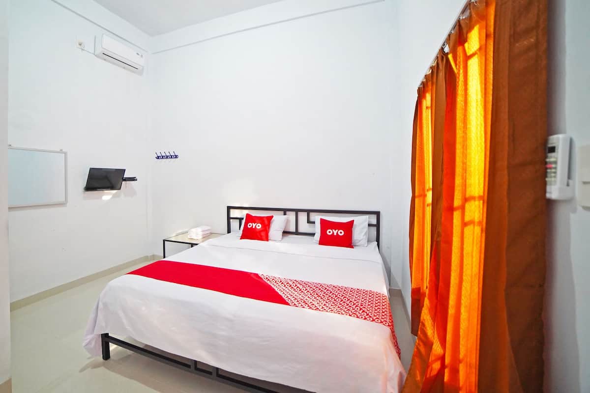 A hotel room with a bed, a bedside table with a phone, a wall-mounted air conditioner, and a window with orange curtains.