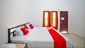 A hotel room with a bed, a nightstand, a red and white bedspread, and two doors with curtains. - OYO 90618 Hanania House Syariah (Langsa)