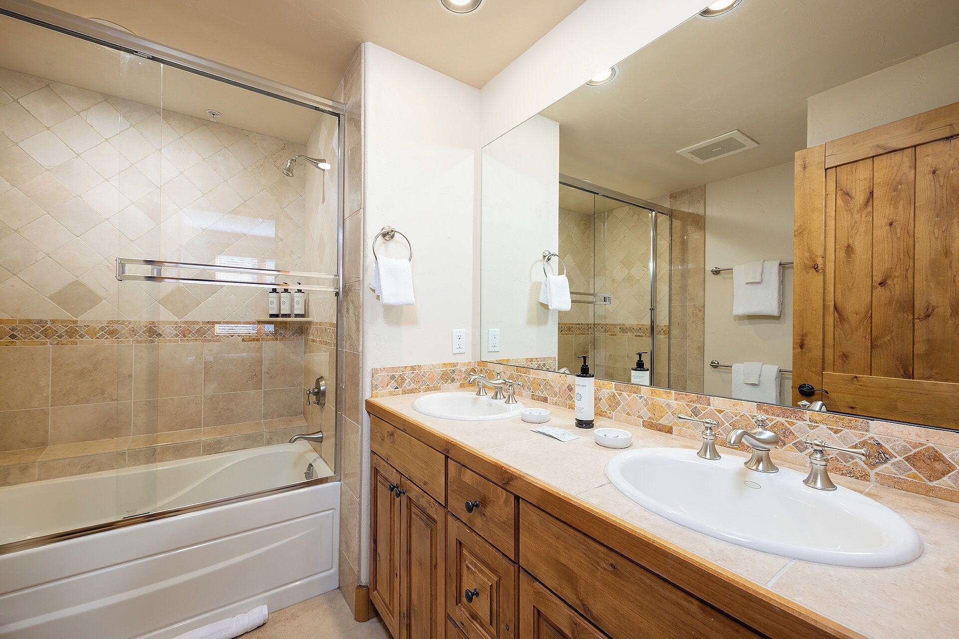 A bathroom with a glass-enclosed shower, two sinks, and a wooden vanity.