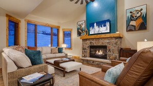 A cozy living room with a stone fireplace, a sofa, a leather armchair, and a coffee table. - AN124 | Antlers Steamboat | Close to Base | A/C | Ski In/Out (Steamboat Springs)