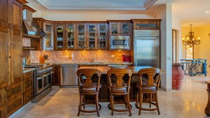 A spacious kitchen with wooden cabinets, a central island with bar stools, a large skylight, and a chandelier. - Pedregal Luxury Villa w/ Infinity Pool, Hot Tub, Walk to Beach & Sunrise Views (Cabo San Lucas)