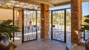 A hotel entrance with stone pillars, a metal gate, and a view of the street and buildings in the background. - Pedregal Luxury Villa w/ Infinity Pool, Hot Tub, Walk to Beach & Sunrise Views (Cabo San Lucas)