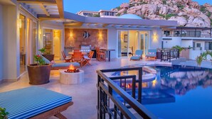 A modern outdoor pool area with a fire pit, lounge chairs, and a dining area. - Pedregal Luxury Villa w/ Infinity Pool, Hot Tub, Walk to Beach & Sunrise Views (Cabo San Lucas)