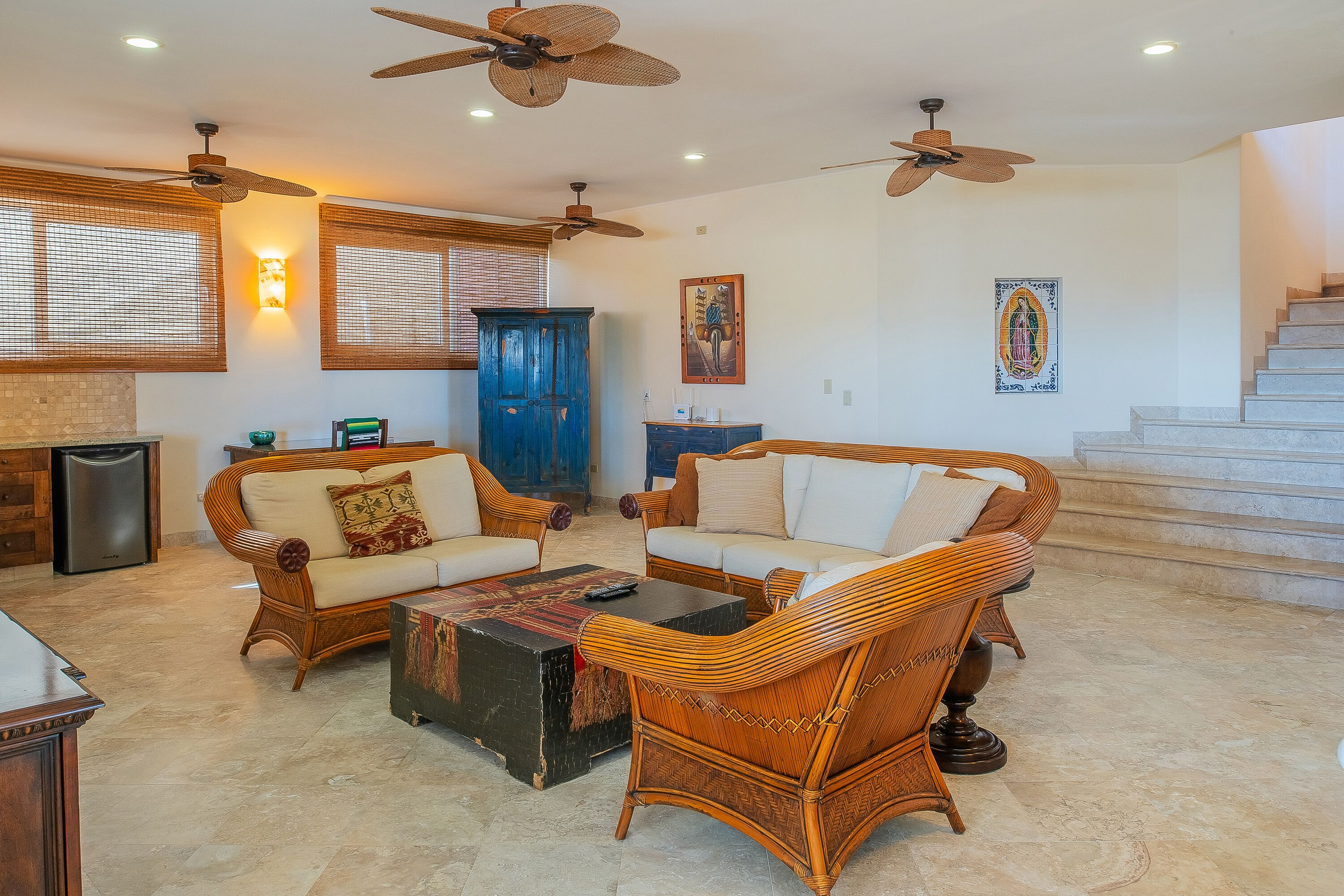 A spacious living room with wicker furniture, ceiling fans, and a staircase leading to an upper level.