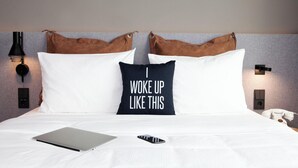 A bed with white bedding, a laptop, a smartphone, and a pillow with text. - Moxy Vienna City East (Vienna)