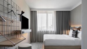 Habitació d'hotel moderna amb un llit, una televisió penjada a la paret, una taula petita i una banca.