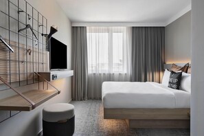 Una habitación de hotel moderna con una cama, un televisor montado en la pared, una mesita y un banco.