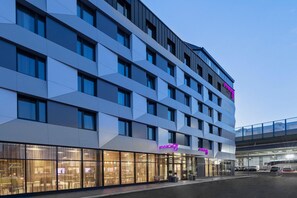 Un hôtel moderne à la façade géométrique, doté de grandes fenêtres et d'une enseigne lumineuse au néon.