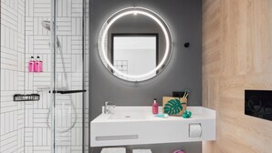 A modern bathroom with a glass-enclosed shower, a white sink with a mirror, and a wooden vanity. - Moxy Vienna City East (Vienna)