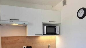 A compact kitchen with white cabinets, a microwave, a coffee maker, and a sink. - Studio Cosy Le 12 (Châlons-en-Champagne)
