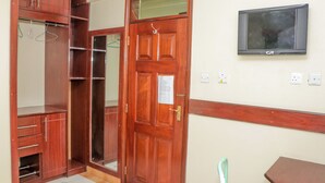 Habitació amb un armari de fusta, una porta, un televisor fixat a la paret i una taula petita.