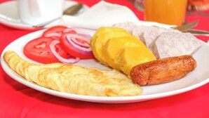 Un plat de petit esmorzar amb una truita, botifarra i tomàquets en rodanxes sobre un mantell vermell.