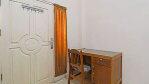 Une pièce avec une porte blanche, un bureau en bois doté de tiroirs, une chaise et un rideau.
