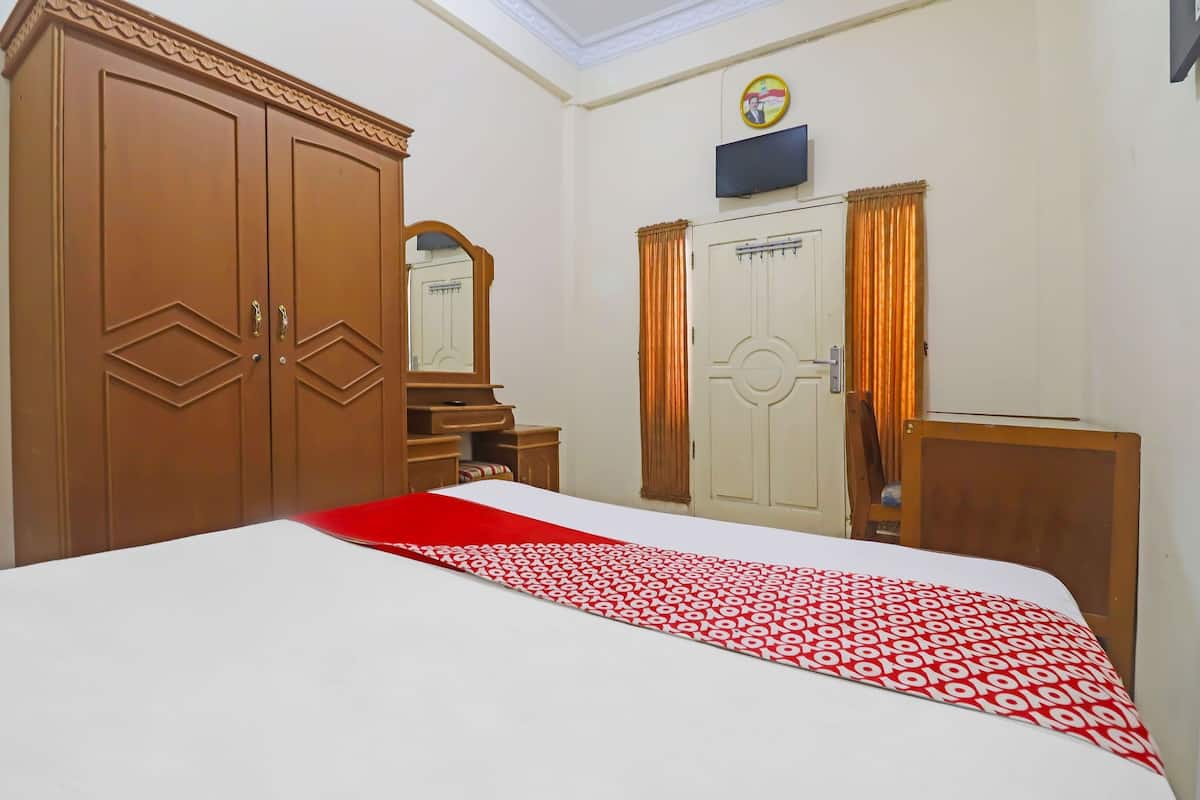 Ein Hotelzimmer mit einem großen Bett, einem Kleiderschrank, einem Spiegel, einem Fernseher und einer Tür mit Vorhängen.