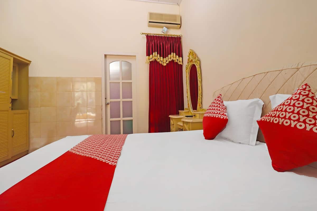 Ein Hotelzimmer mit einem großen Bett, rot-weißer Bettwäsche, einem Spiegel und einem roten Vorhang.