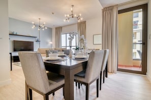 A dining area with a dark wooden table, four chairs, a chandelier, and a television in the background.