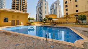 A swimming pool with a tiled deck, surrounded by high-rise buildings and a yellow building with a sign.