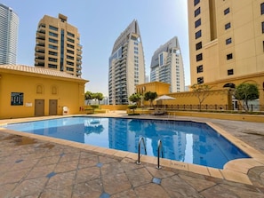 A swimming pool with a tiled deck, surrounded by high-rise buildings.
