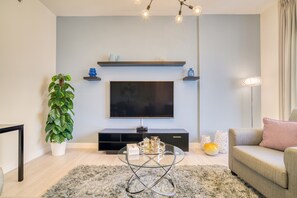 A modern living room with a flat-screen TV, a glass coffee table, a potted plant, a sofa, and a floor lamp.