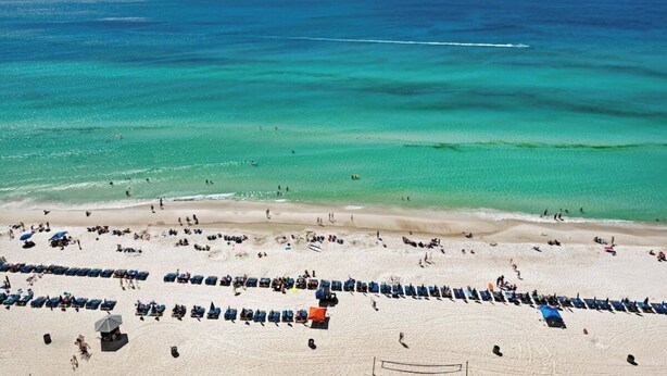 Una playa con filas de tumbonas y sombrillas, una red de voleibol y una vista despejada del océano.