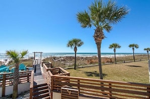 A wooden boardwalk leading to beach chairs and a palm tree-lined path.