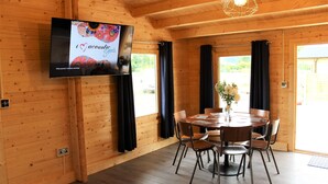 A wooden interior with a round dining table, chairs, a television mounted on the wall, and a window with curtains. - Inviting 3-bedroom Lodge in Ashton Under Hill (Evesham)
