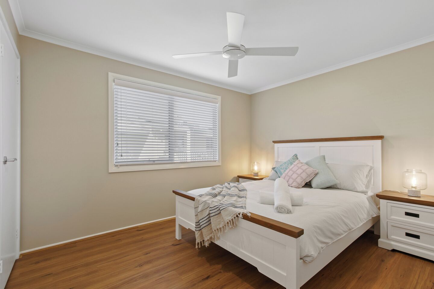 Ein Schlafzimmer mit Bett, Nachttischen, Deckenventilator und Fenster mit Jalousien.