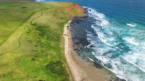 Vue aérienne d’un paysage côtier comprenant une plage, des zones herbeuses et l’océan.