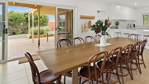 Une cuisine moderne avec des meubles blancs, un coin repas avec une table et des chaises en bois, et une porte-fenêtre coulissante donnant sur une terrasse verdoyante.