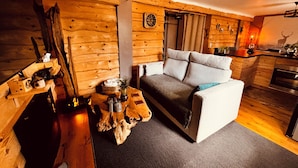 Ein gemütliches Blockhaus-Interieur mit Holztisch, einer Couch und einer Küchenzeile.