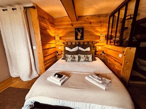 Een gezellig houten blokhut slaapkamer met een bed, twee bedlampen, een nachtkastje en een houten hoofdbord.