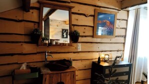 Ein rustikales Blockhaus-Interieur mit einem Holzbecken, einem Spiegel, einem Hirschbild in einem Rahmen und einer kleinen Weihnachtstanne.