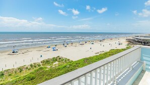 A beach view from a balcony with a wooden railing, a sandy beach, and a pier with umbrellas. - Private Beachfront Home w/ 5 Decks, 3 Suites, Fenced Yard in Beachside Village (Galveston)