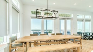 A spacious dining area with a large wooden table, benches, and a modern pendant light. - Private Beachfront Home w/ 5 Decks, 3 Suites, Fenced Yard in Beachside Village (Galveston)
