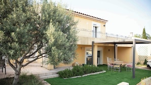 Une maison à deux étages avec un balcon, une terrasse dotée d’une table et de chaises, et une pelouse bien entretenue.