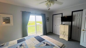 A bedroom with a large bed, a ceiling fan, a TV mounted on the wall, and a view of a grassy area through a sliding door. - Captain's Quarters -Water Front- Water Access-Pet Friendly-NO LINENS (Chincoteague)