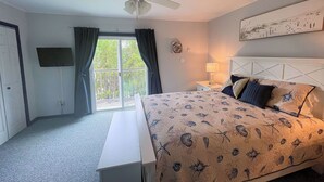 A bedroom with a bed, a nightstand, a ceiling fan, a window with curtains, and a view of trees outside. - Captain's Quarters -Water Front- Water Access-Pet Friendly-NO LINENS (Chincoteague)