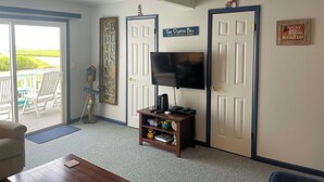 A living room with a TV, a wooden sign, and a door to an outdoor area. - Captain's Quarters -Water Front- Water Access-Pet Friendly-NO LINENS (Chincoteague)