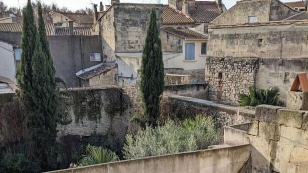 Une terrasse sur le toit, avec des murs en pierre, des plantes en pot et une table entourée de chaises.