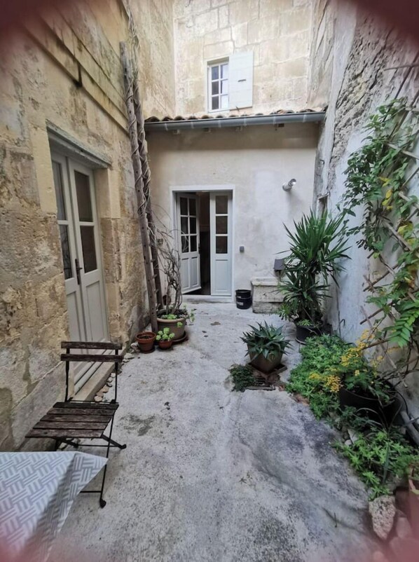 A narrow courtyard with a rustic stone wall, a wooden bench, and potted plants.