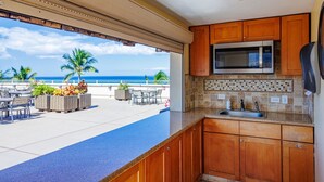 A kitchen with a view of the ocean, outdoor seating, and a stone backsplash. - Royal Mauian #219 2 Bedroom Condo by RedAwning (Kihei)