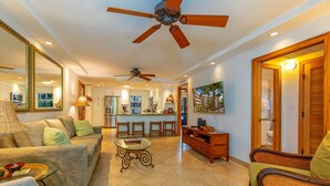 A spacious living room with a ceiling fan, a dining area with a bar, and a kitchen in the background. - Royal Mauian #219 2 Bedroom Condo by RedAwning (Kihei)