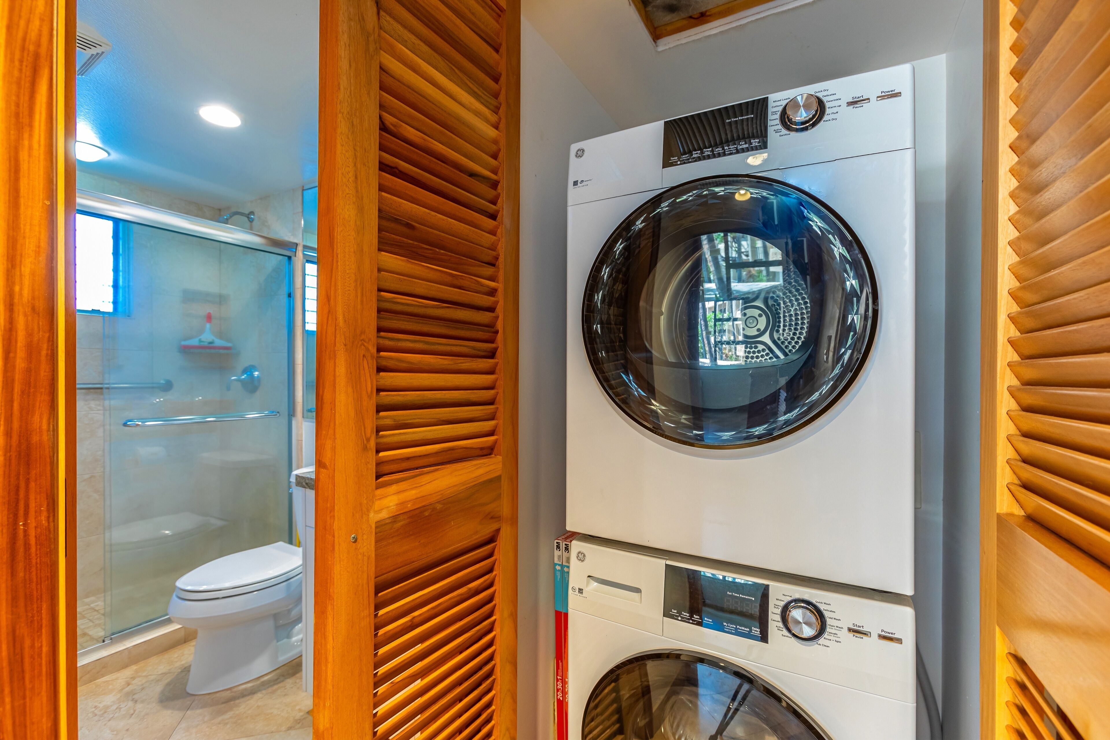 A compact, modern bathroom with a built-in washer and dryer, a glass shower enclosure, and a toilet.