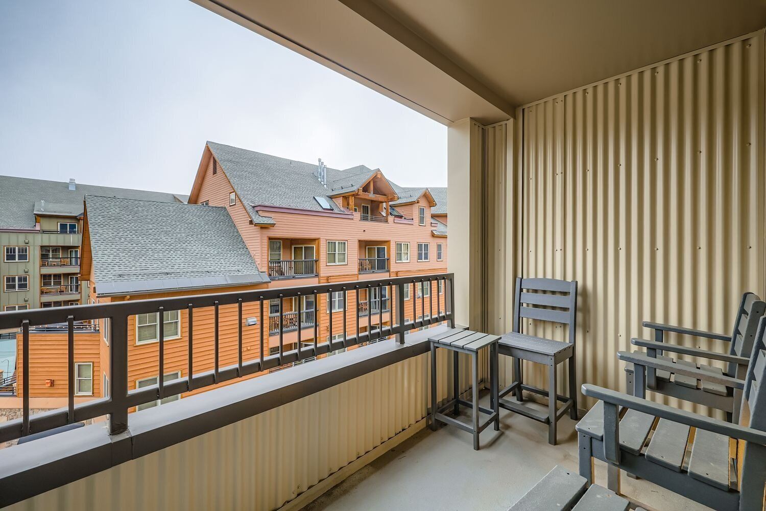 A balcony with a view of neighboring buildings, a metal railing, and a table with chairs.