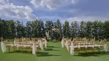 Rows of golden chairs with white cushions, arranged on a green carpet, facing a decorated archway with floral arrangements.