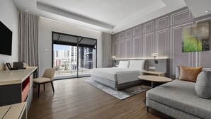 A modern hotel room with a large bed, a desk, a sofa, and a view of the city.