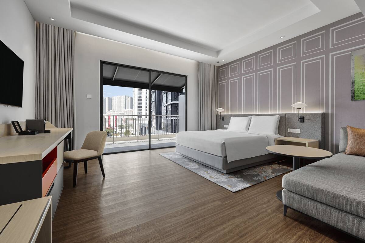 Habitación de hotel moderna con una cama grande, un escritorio, un sofá y vistas a la ciudad.